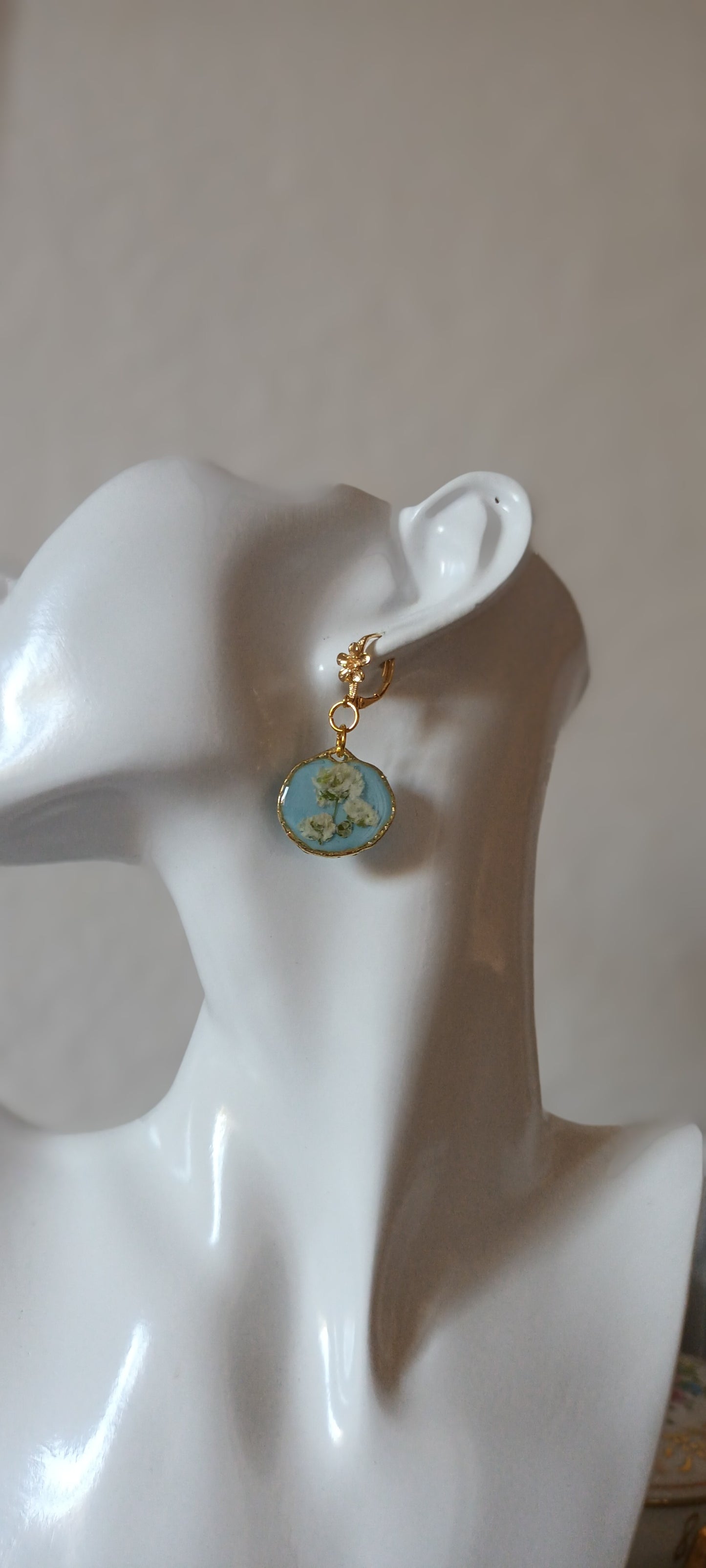 boucles d'oreilles en résine sur fond bleu ciel et fleurs blanches pressées