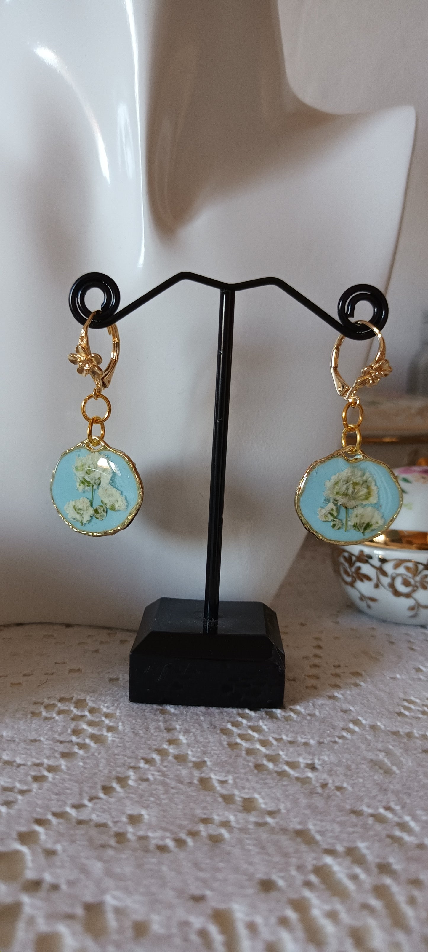boucles d'oreilles en résine sur fond bleu ciel et fleurs blanches pressées