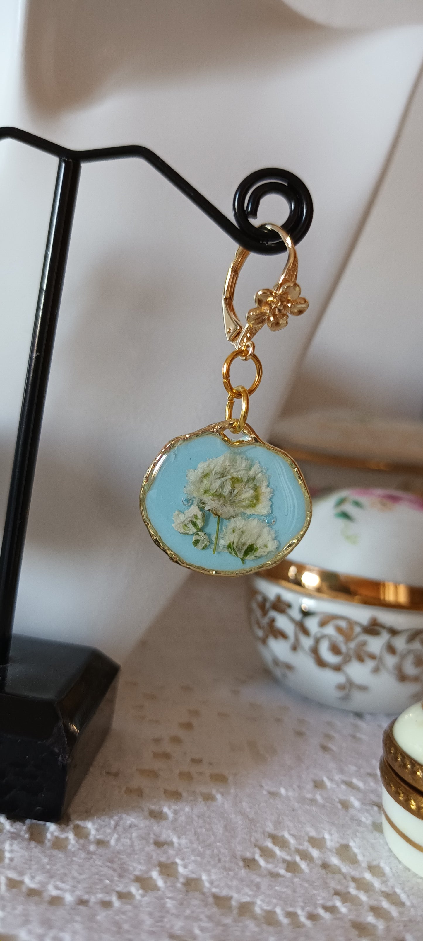 boucles d'oreilles en résine sur fond bleu ciel et fleurs blanches pressées